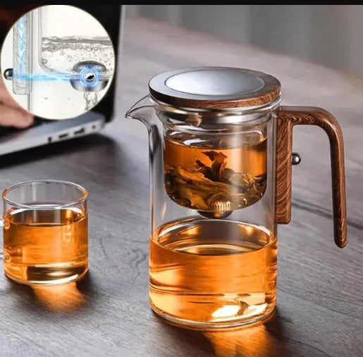 Glass teapot with wooden handle and a small glass cup on a wooden surface.