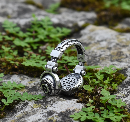 Silver headphone-shaped keychain on a stone surface with greenery