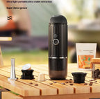 Black portable coffee maker on a wooden surface with coffee beans and a package in the background.