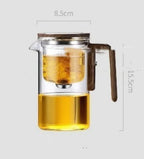 Glass teapot with wooden handle filled with tea, showing dimensions on a white background