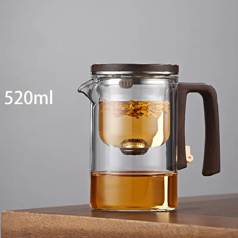 Clear glass teapot with brown handle and lid filled with tea on a gray background